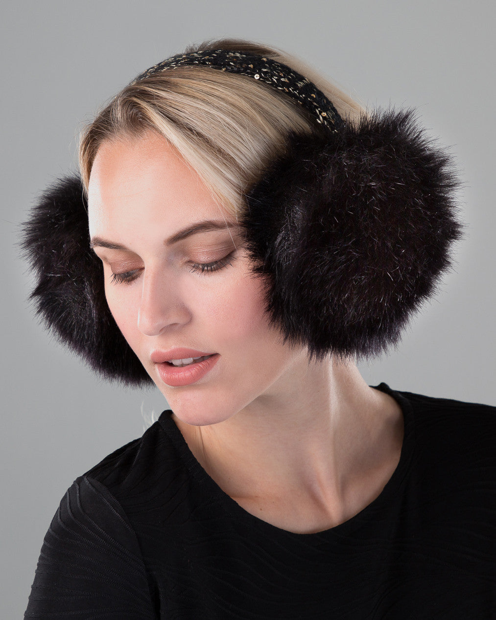 Blonde woman in black shirt is wearing a pair of grey fox fur earmuffs with a black velvet band.