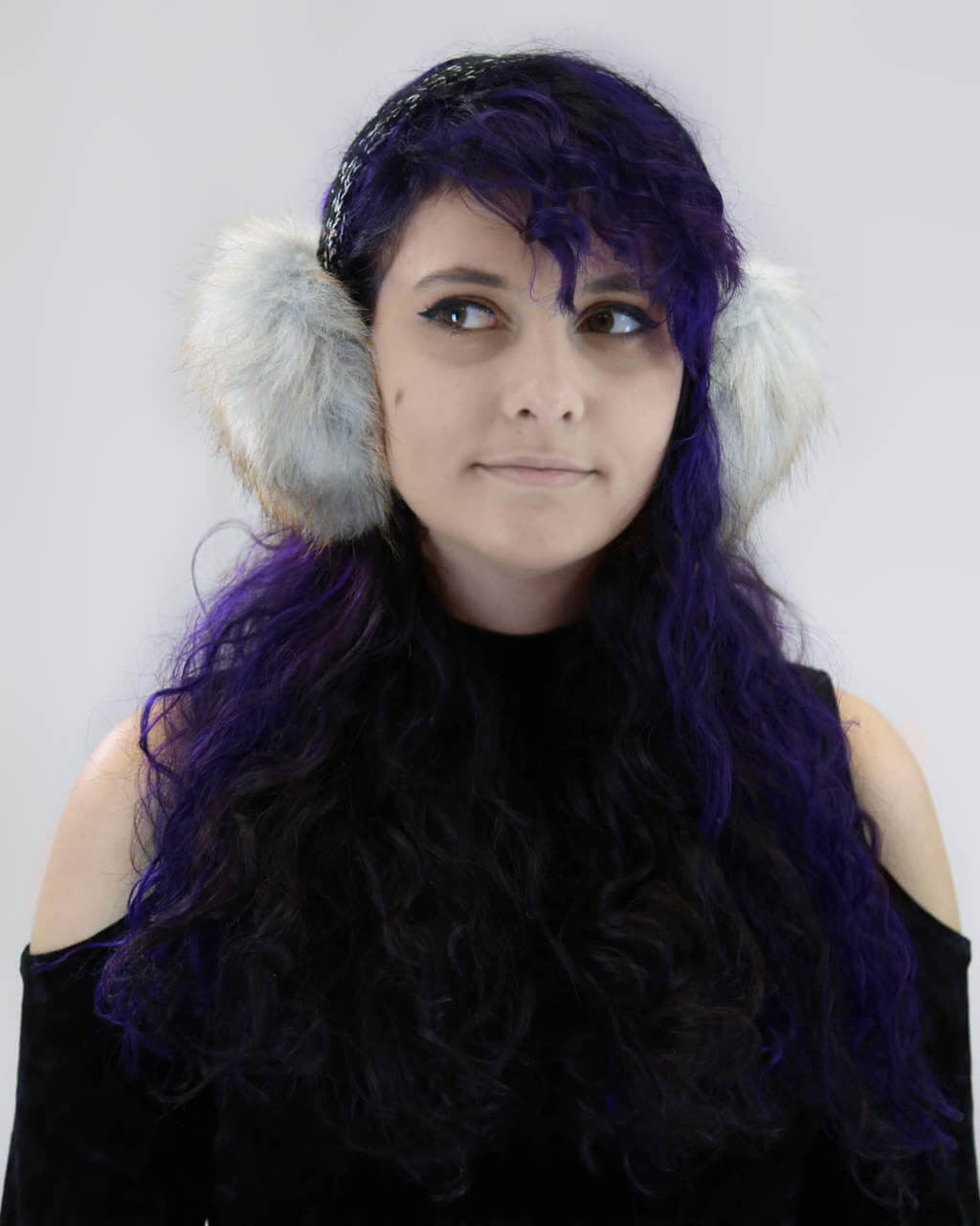 A woman is wearing a pair of natural blue faux fox fur earmuffs with a tan bling band.
